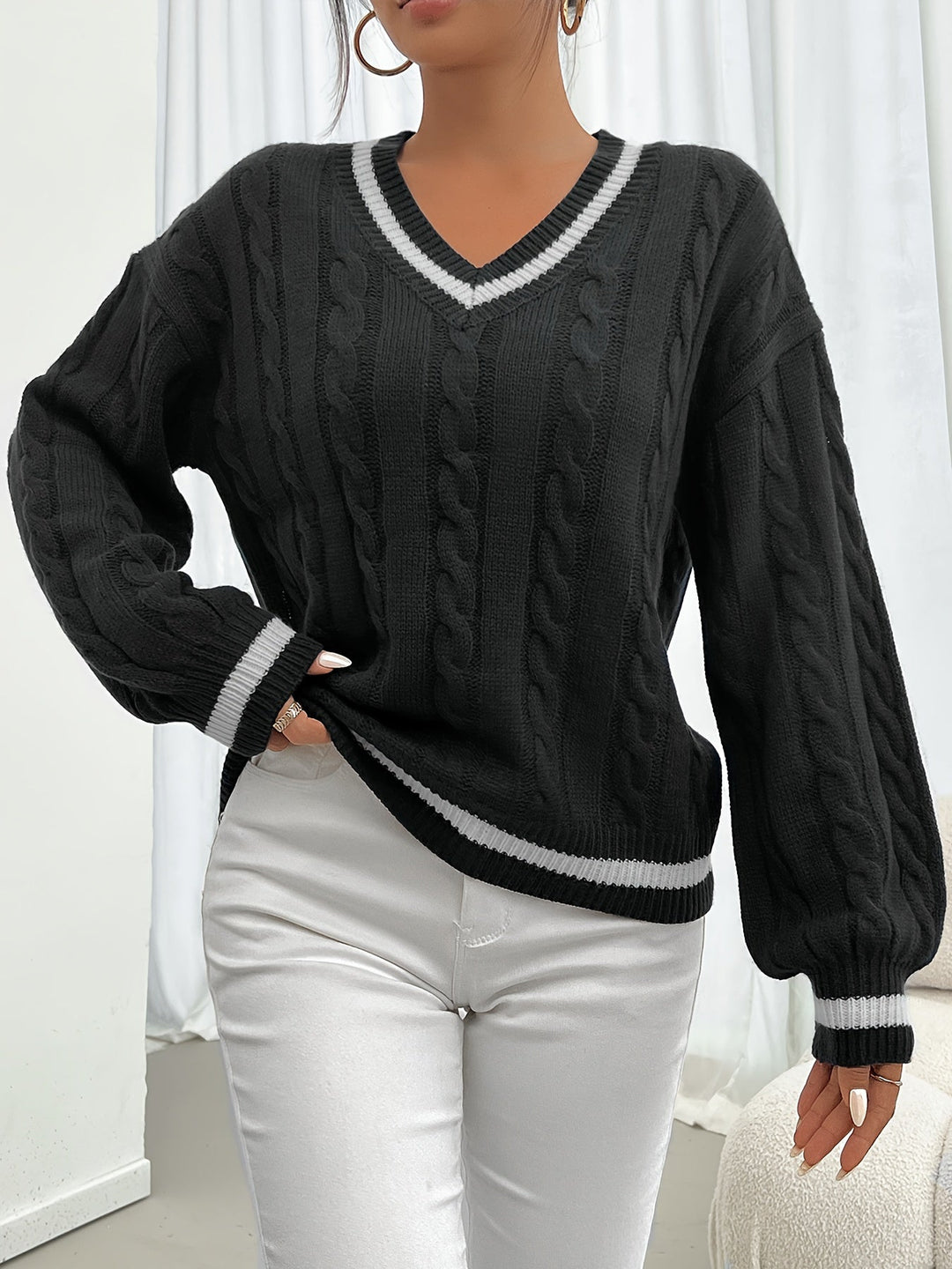 Woman wearing black cable-knit V-neck oversized sweater, holding coffee cup