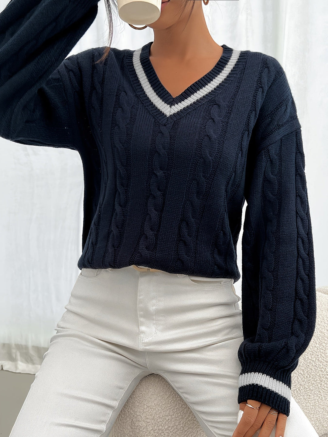 Woman wearing black cable-knit V-neck oversized sweater with striped trim, front view