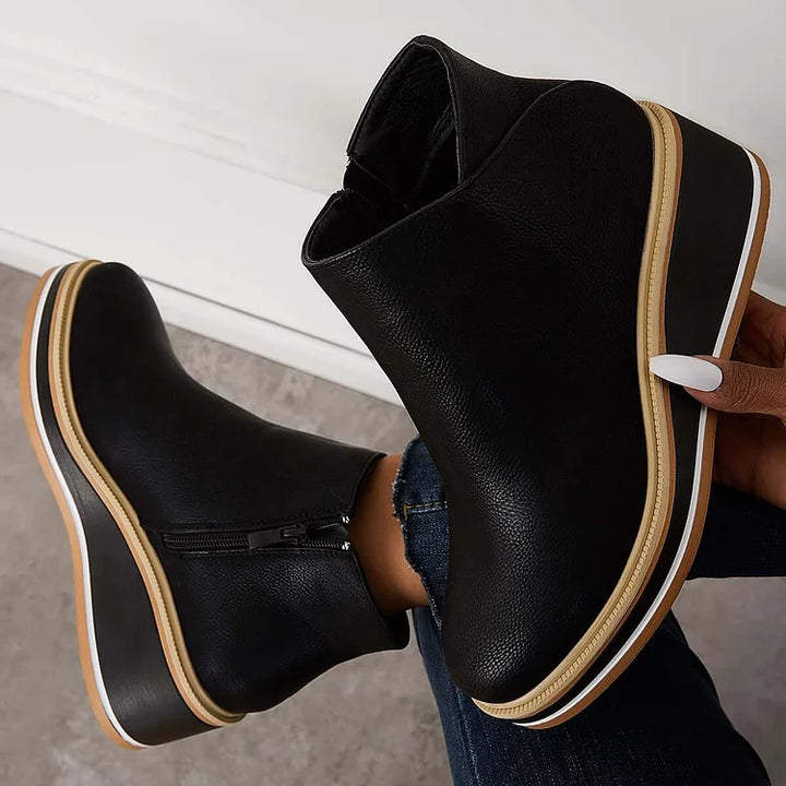 Harlow black wedge ankle boots held by hand showing platform sole