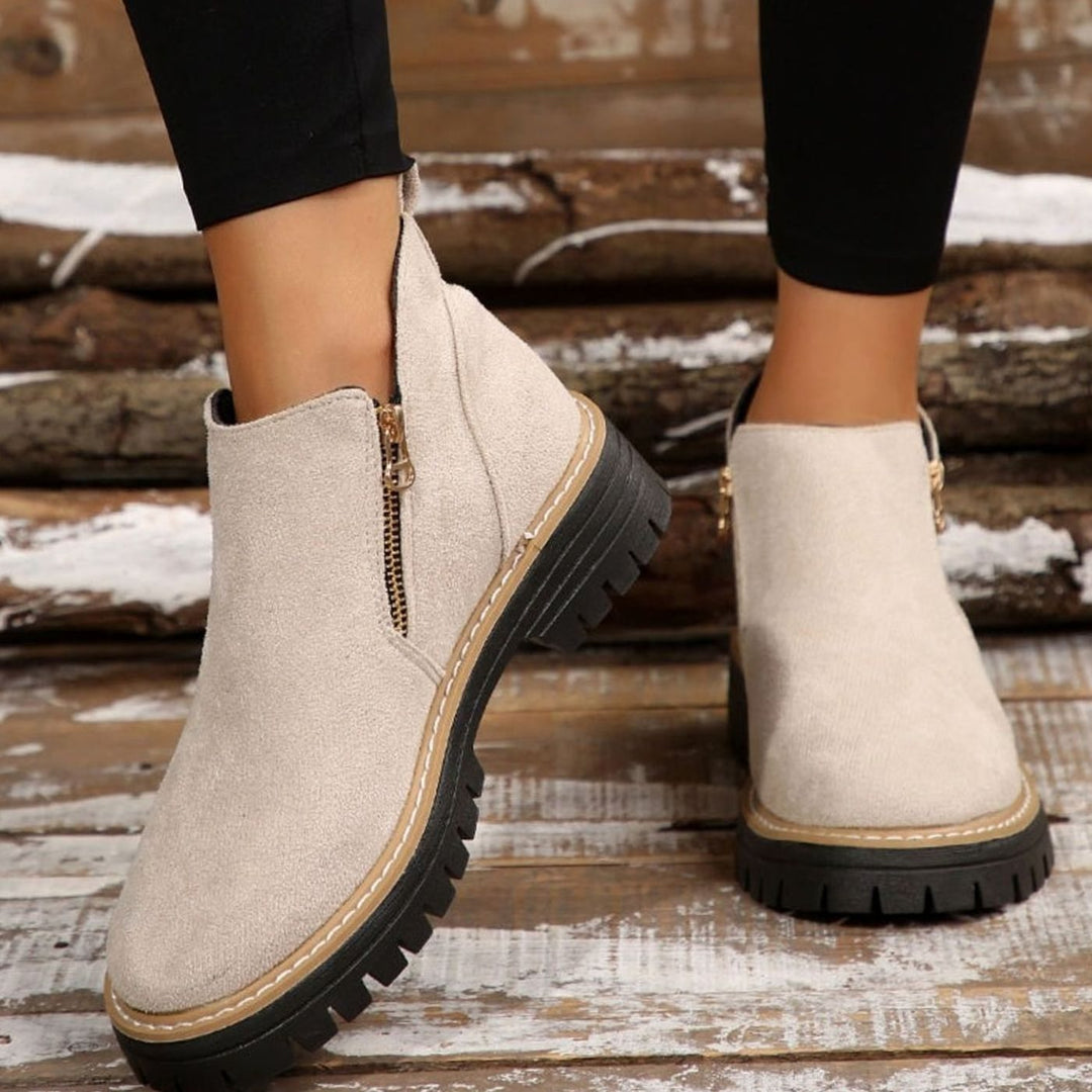 Beige platform ankle boots with gold zipper, held by hand