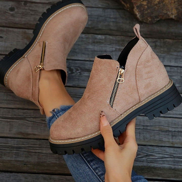 Beige platform ankle boots with gold zipper, held by hand