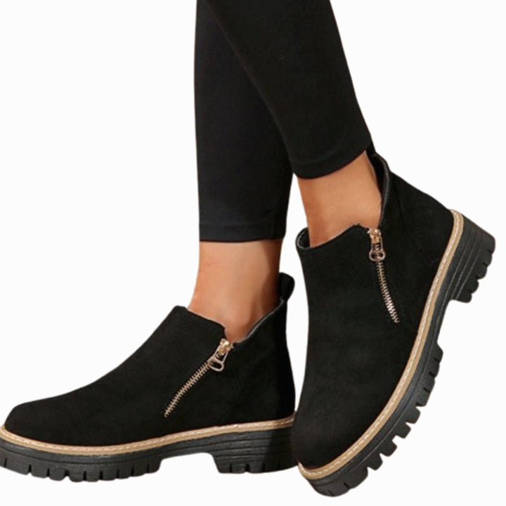 Black suede-look ankle boots with gold zipper, side view on model