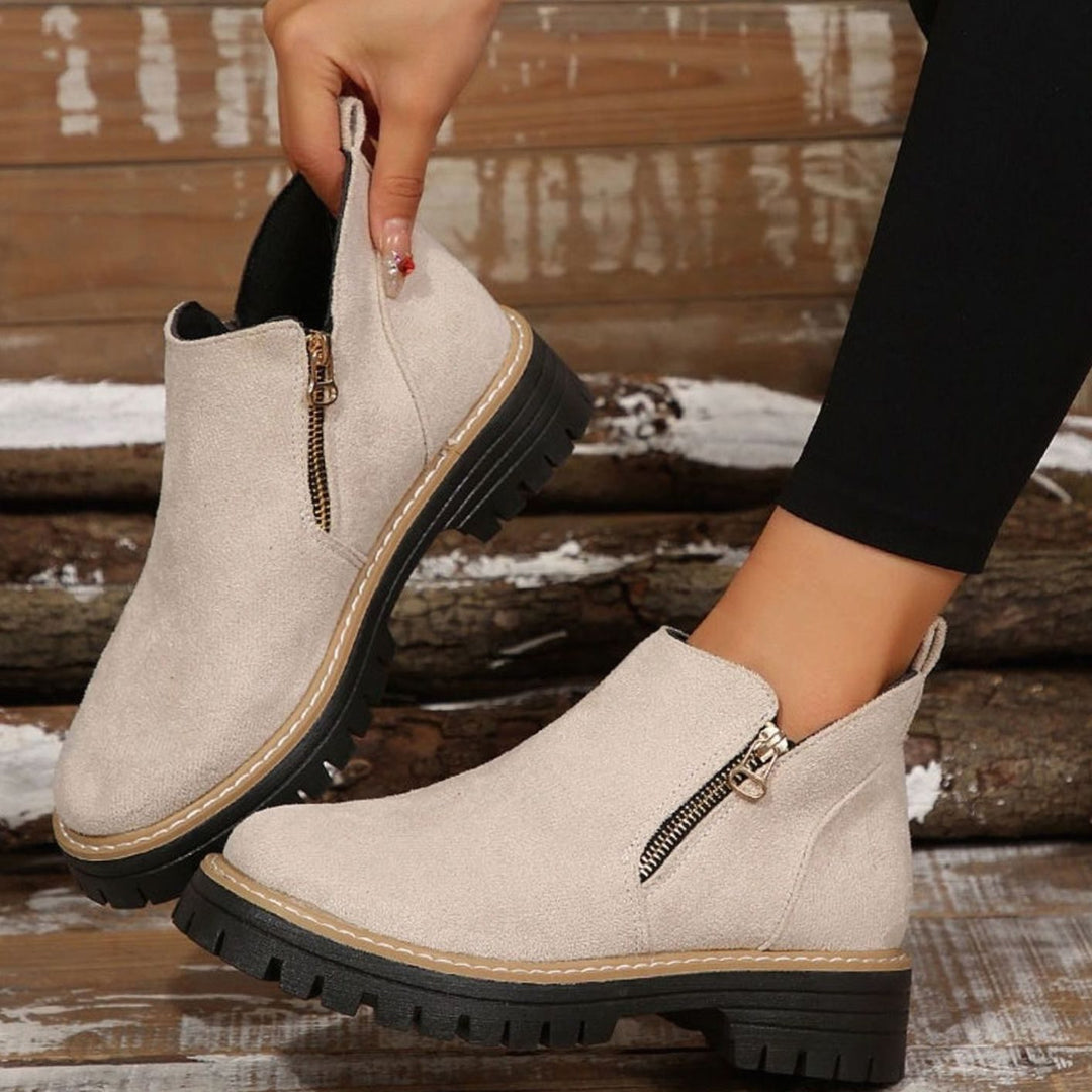 Beige platform ankle boots with gold zipper, held by hand