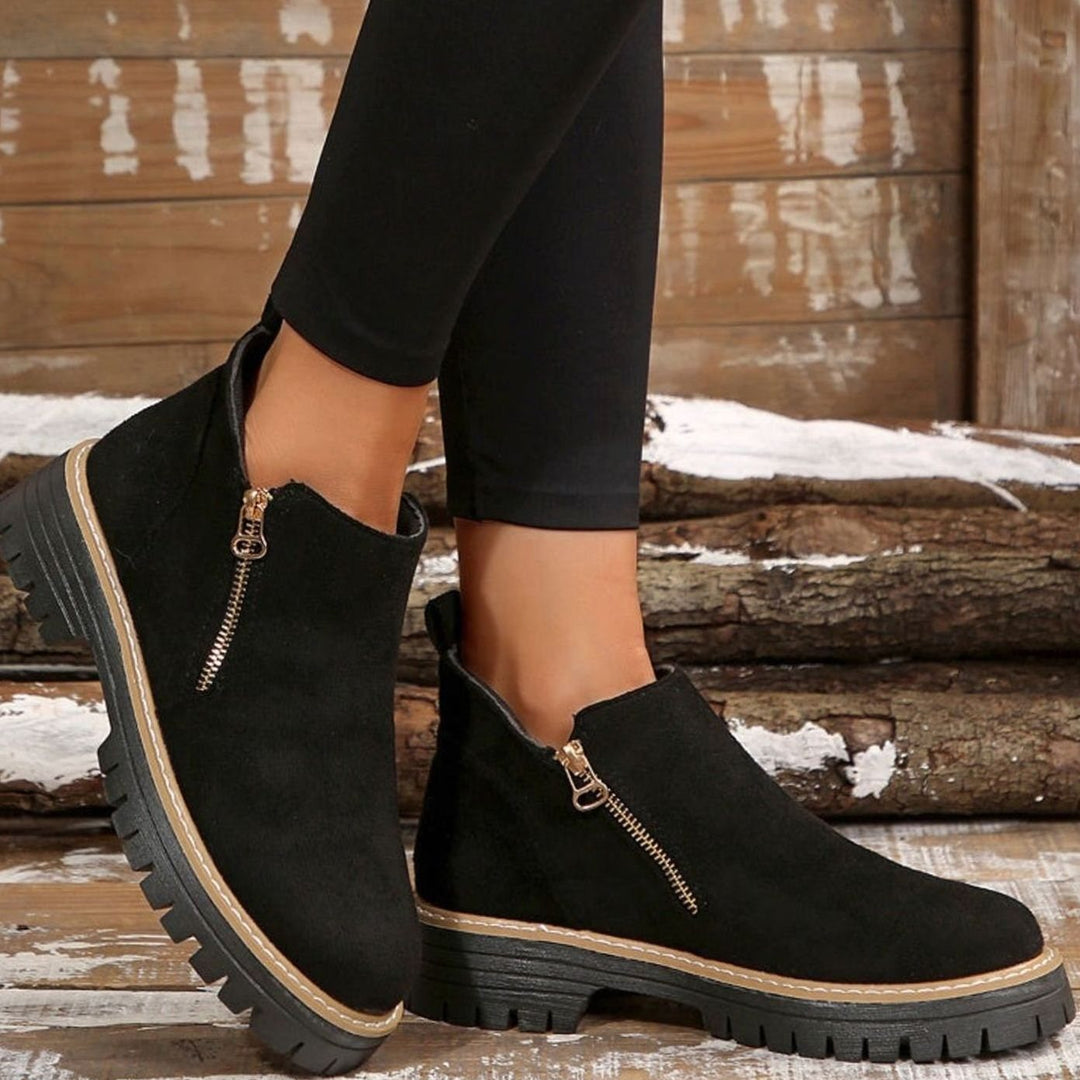 Beige platform ankle boots with gold zipper, held by hand