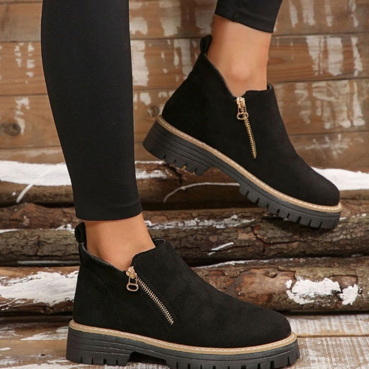 Beige platform ankle boots with gold zipper, held by hand