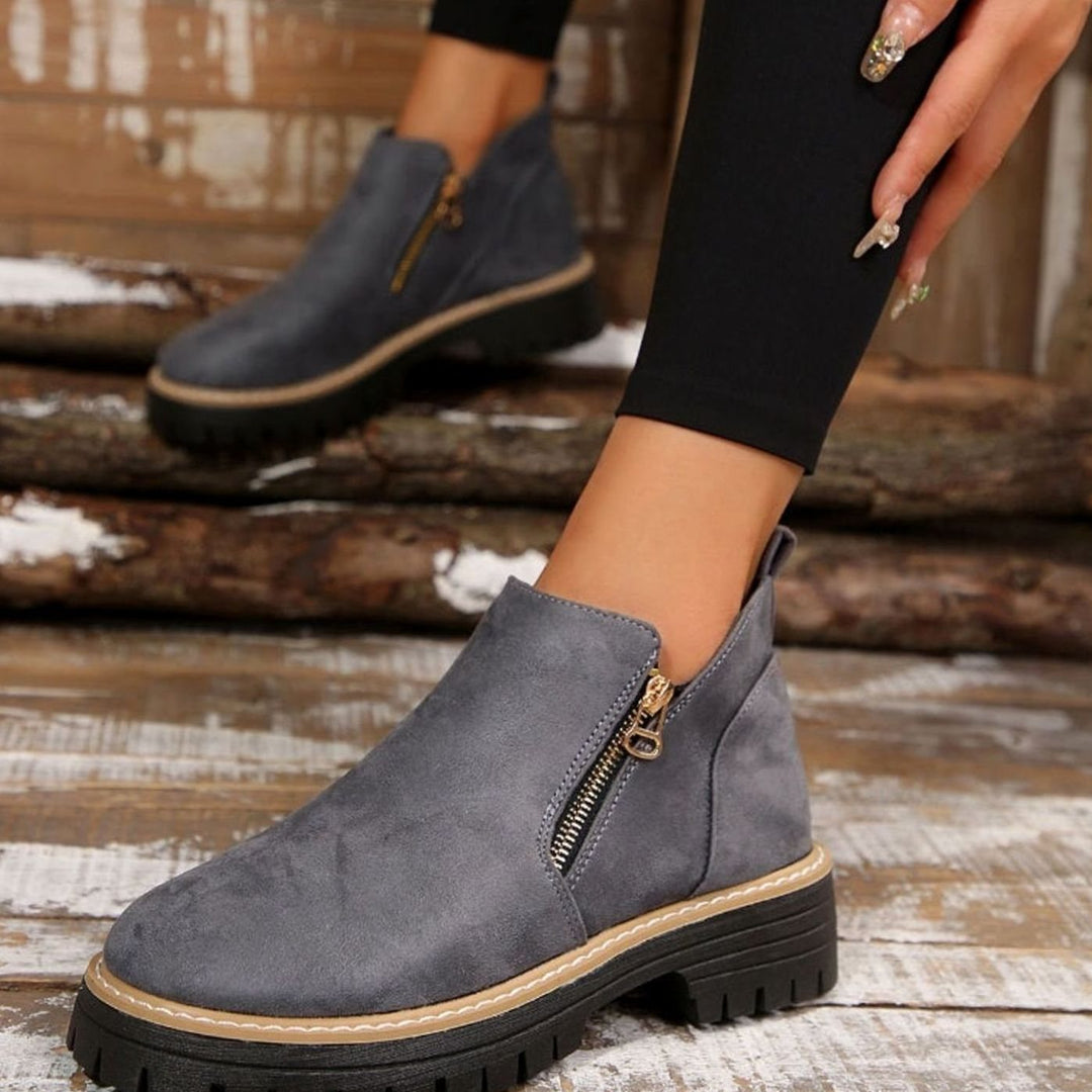 Beige platform ankle boots with gold zipper, held by hand