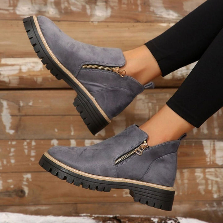 Beige platform ankle boots with gold zipper, held by hand