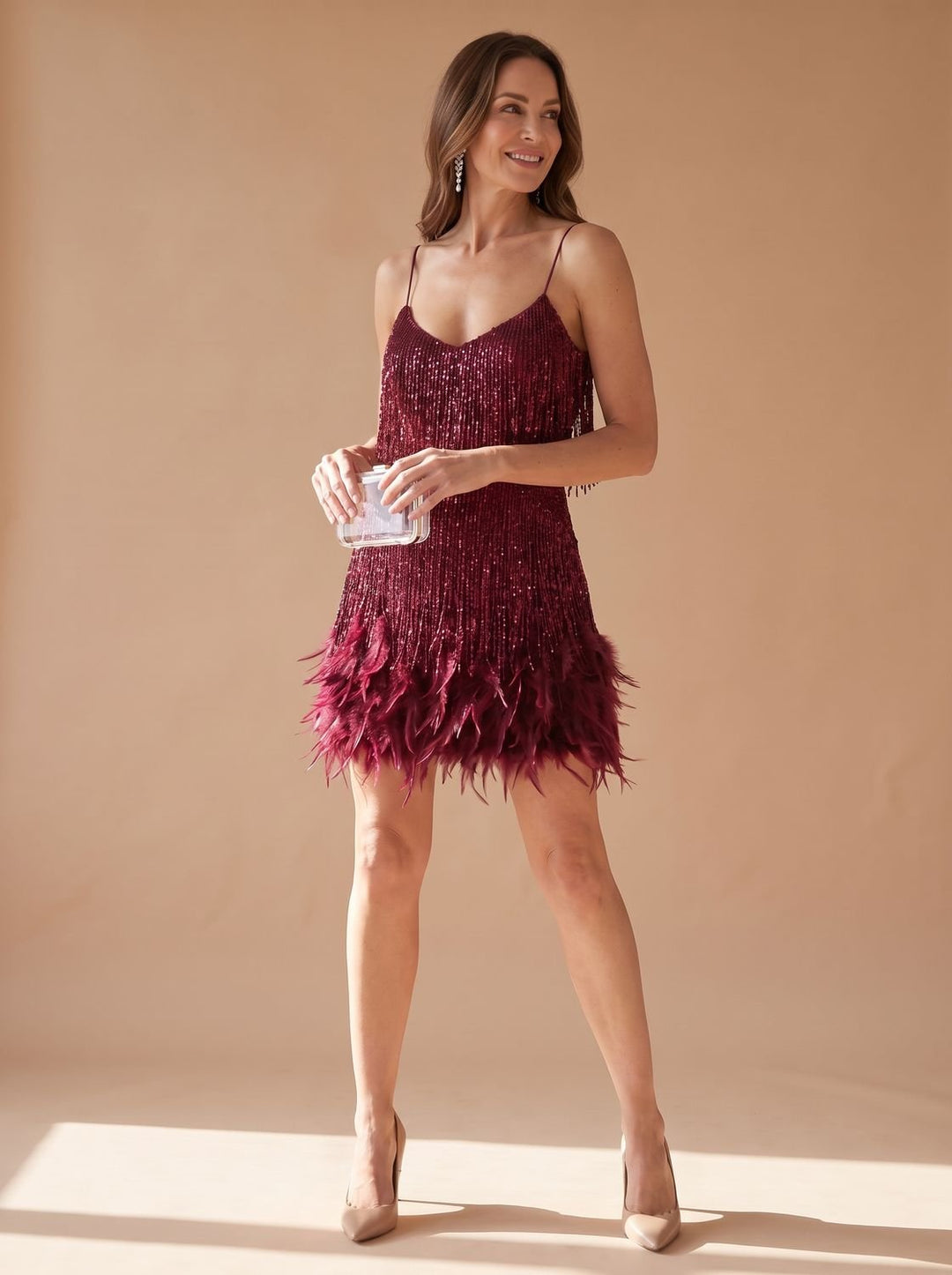 Vespera sequin mini dress with feather fringe hem, side view holding clutch, wine red