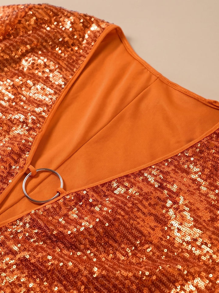 Close-up of gold ring detail on orange sequin plunge-neck dress