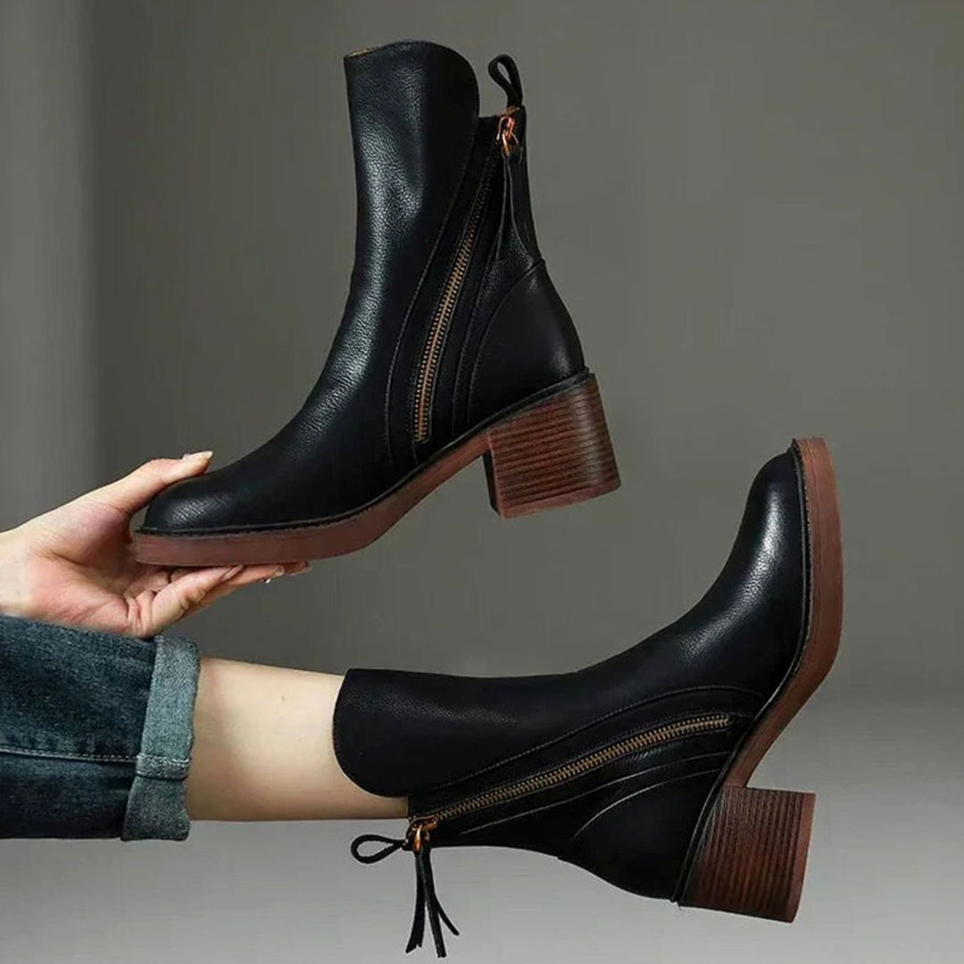 Marguerite black block heel ankle boots held by hand, side view